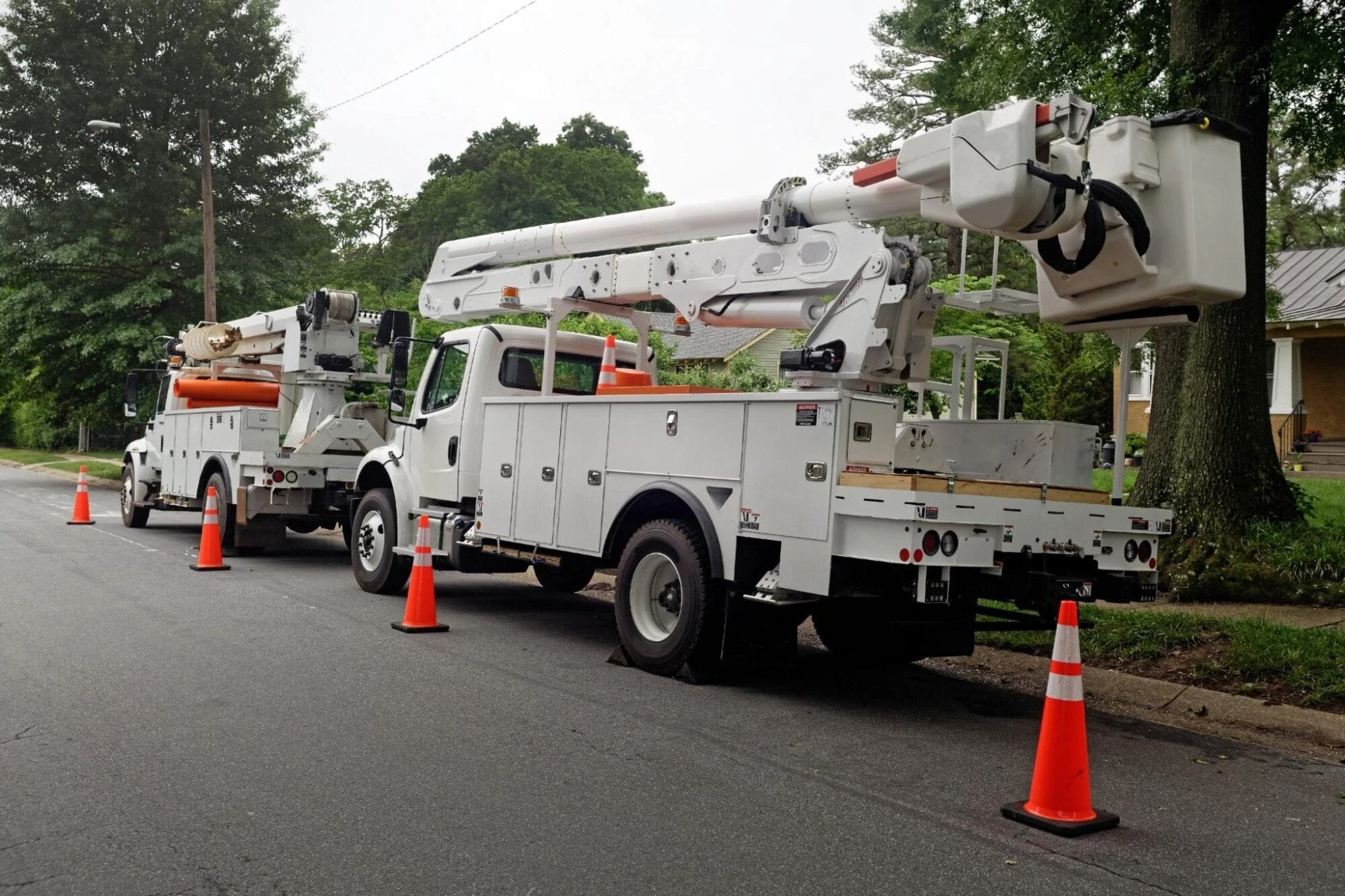 Two white utility bucket trucks are parked on a residential street Two white utility bucket trucks are parked on a residential street